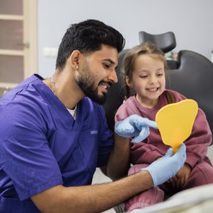 Orthodontist in Monrovia showing a young patient her smile in a hand mirror during a friendly dental visit